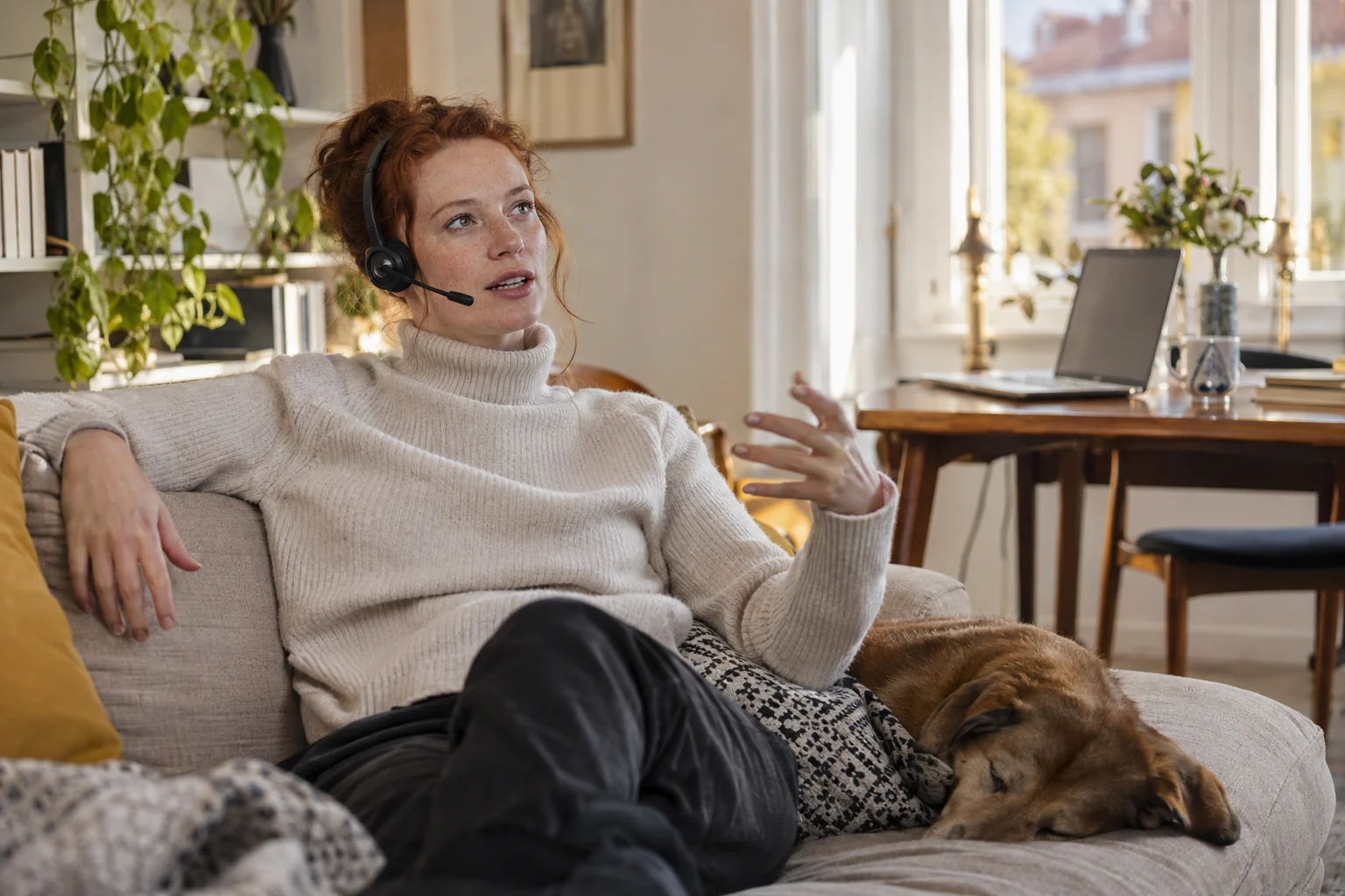 KI-generierte Szene: Eine Person diktiert entspannt auf dem Sofa mit Headset; der offene Laptop steht hinten rechts.